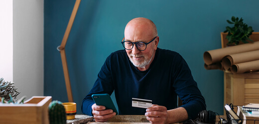 A man seated using his credit card and smart phone.