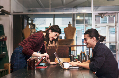 A woman leans over a table to look at laptop computer