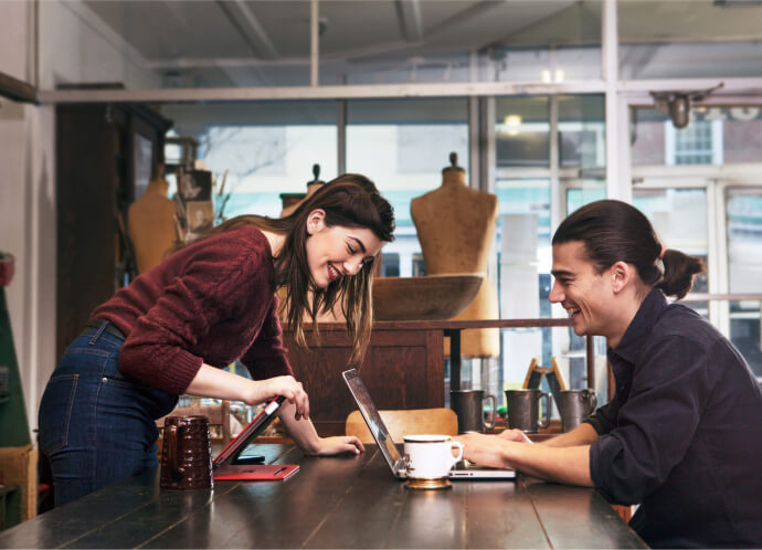 A woman leans over a table to look at laptop computer