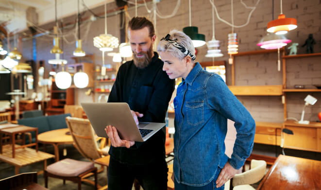 A man and woman standing while looking at an open laptop computer