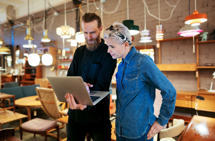 A man and woman standing while looking at an open laptop computer
