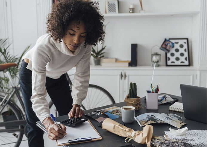 A woman leans down to write on a notepad on a coffee table