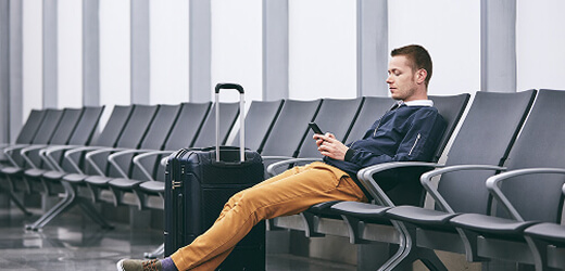A man sits on a bench at the airport looking over his phone