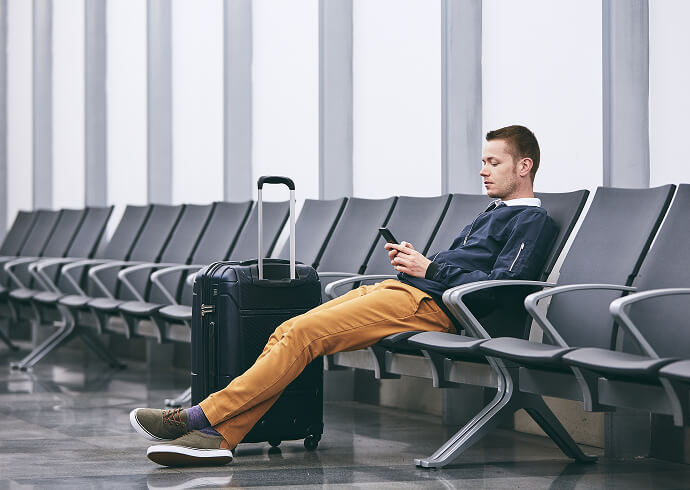 A man sits on a bench at the airport looking over his phone