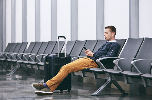 A man sits on a bench at the airport looking over his phone