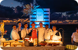 A group of the chefs attending the Cayman Cookout 2023 pose for a photo at sunset
