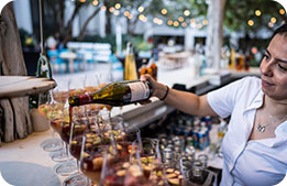 A bartender filling a row of glasses with red wine