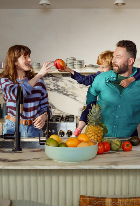 A couple and their young son enjoy fruit in their kitchen