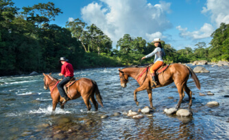 Two horseback riders cross a small stream