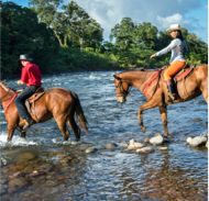 Two horseback riders cross a small stream