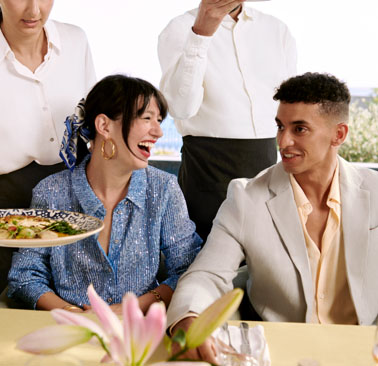 Two guests sit side-by-side at a table as a server places a dish in front of them