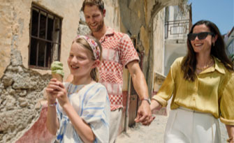 Little girl eats an ice cream cone while walking with parents.