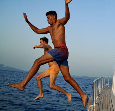 Two men jumping off a boat while woman watches