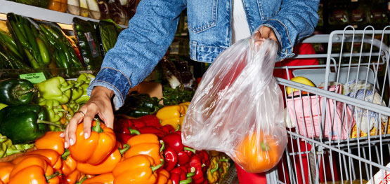 A grocery shopper adds an orange bell pepper into a plastic bag