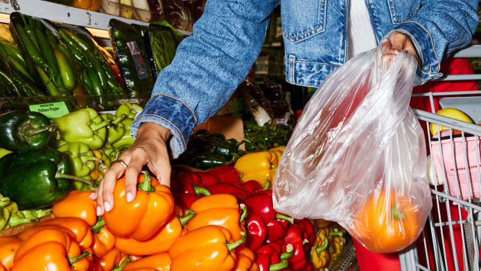 A grocery shopper adds an orange bell pepper into a plastic bag