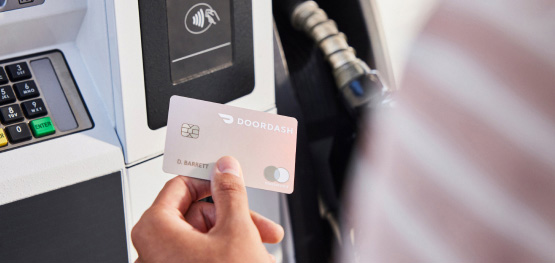 A cardmember uses her DoorDash Credit Card at a gas station pump