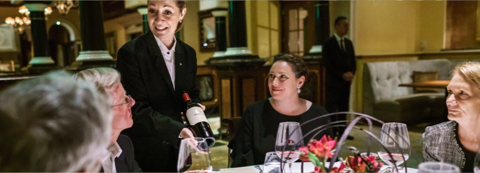 A server presenting wine to guests seated at a table