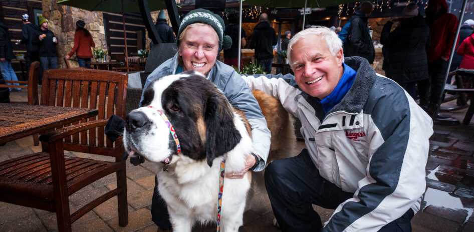 Two guests pose with a dog during apres ski activities