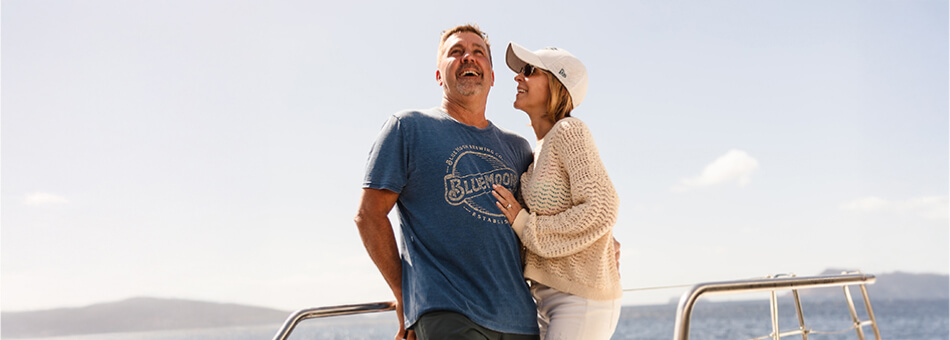Couple embracing on a balcony with a scenic view of the sea and sunset.