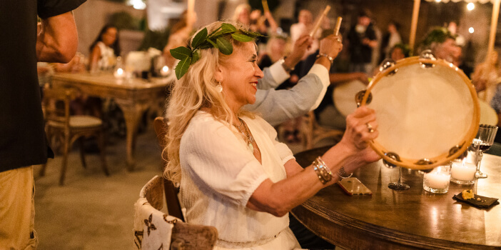 Woman smiling, playing a tambourine in a festive crowd.