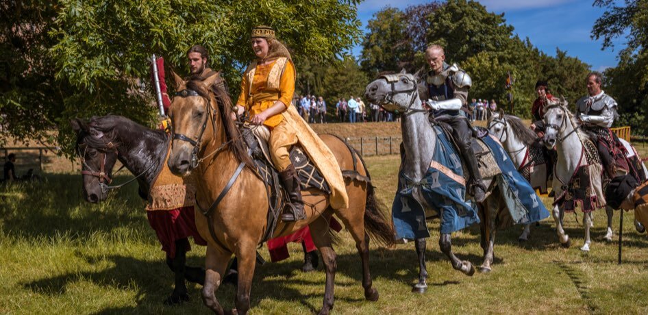 Actors and actresses ride horses in a Renaissance festival setting
