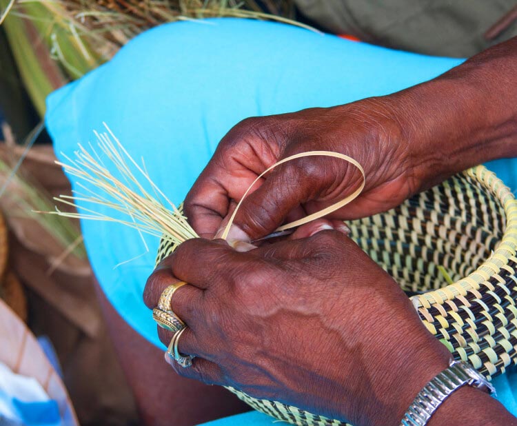A close-up shot of hands weaving a basket together, using natural textiles and fibers