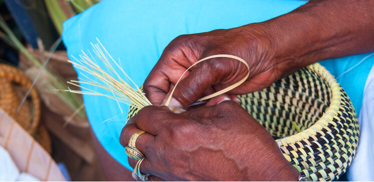 A close-up shot of hands weaving a basket together, using natural textiles and fibers