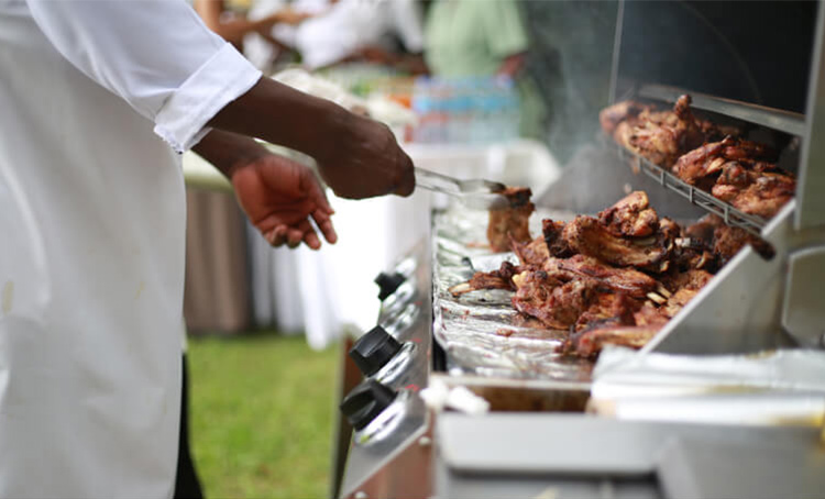 A Caribbean chef cooks chicken over an outdoor grill