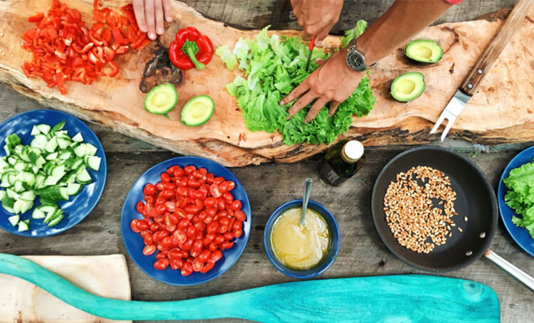 An overhead shot of Native American hands preparing peppers, avocados, greens, and dressing on an outdoor setting
