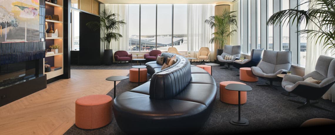 Modern Sapphire Lounge at Boston Logan International Airport with curved leather sofas, armchairs, small tables, and large windows with runway views.