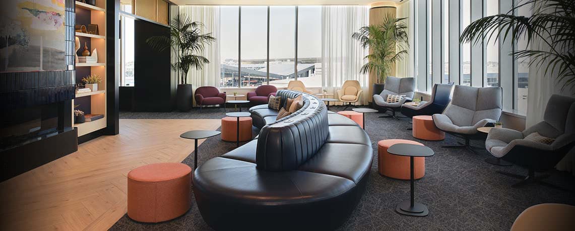 Modern Sapphire Lounge at Boston Logan International Airport with curved leather sofas, armchairs, small tables, and large windows with runway views.