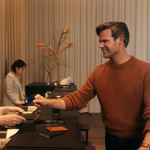 A man in an orange sweater smiling while handing his card over