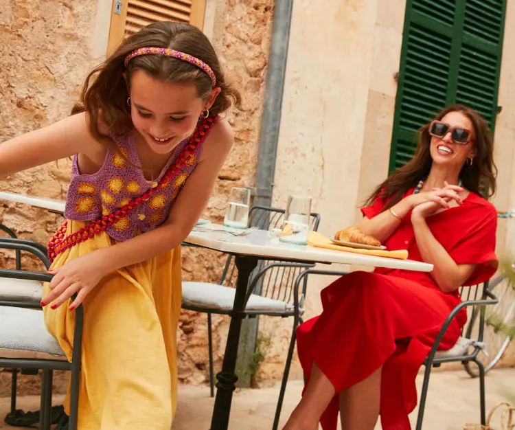 Mother and daughter sitting outdoors near a building with stone walls and green shutters