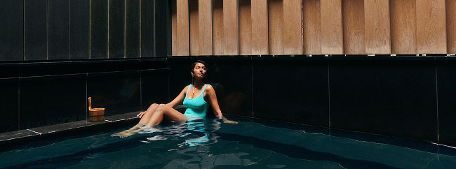 A person in a green swimsuit relaxing in a pool in Japan, leaning against the edge.