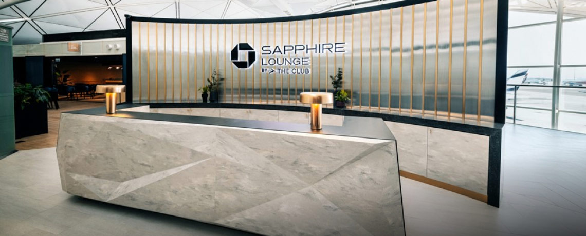 Reception area of the Sapphire Lounge at Hong Kong International Airport with a sleek stone desk, gold bars, and the lounge logo.