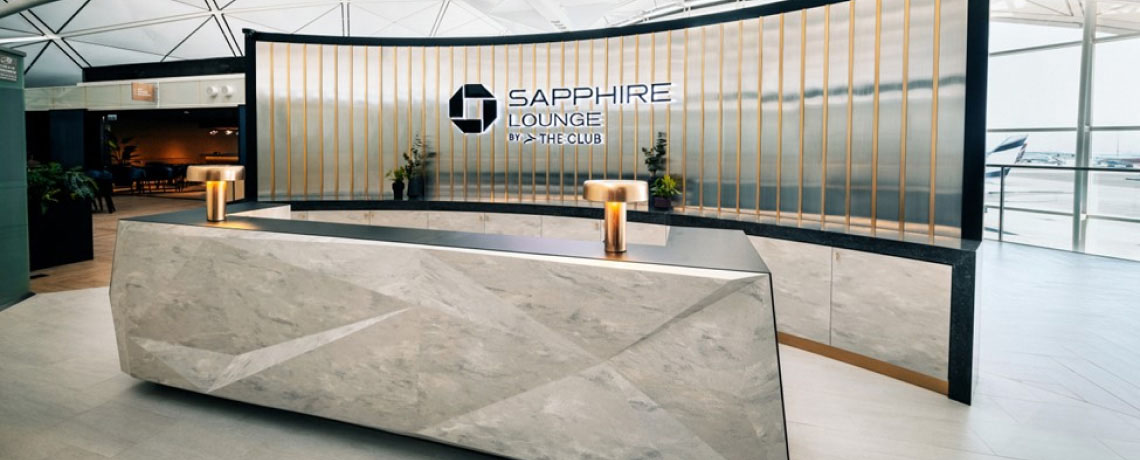 Reception area of the Sapphire Lounge at Hong Kong International Airport with a sleek stone desk, gold bars, and the lounge logo.