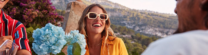 A person outdoors, with blue hydrangea flowers in the foreground and scenic hills or mountains in the background.