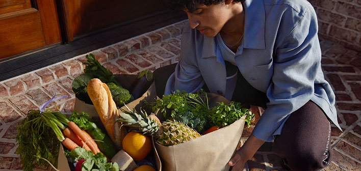 Person picking up bags filled with fresh produce and groceries.