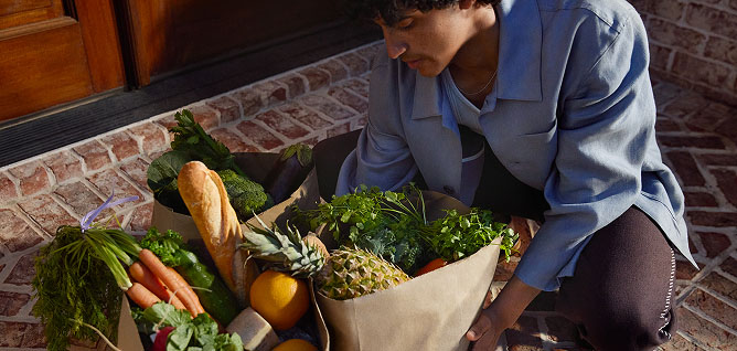 Person picking up bags filled with fresh produce and groceries.
