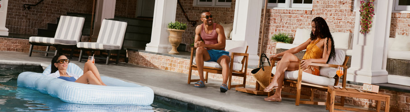 Three people relaxing poolside, with one person floating in the pool.