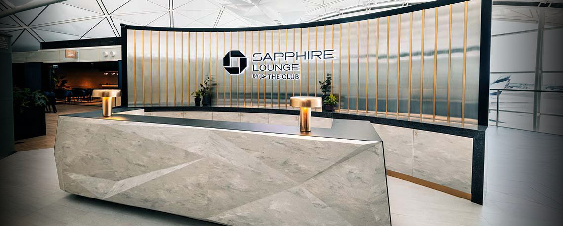 Reception area of the Sapphire Lounge at Hong Kong International Airport with a sleek stone desk, gold bars, and the lounge logo.