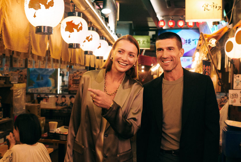 Two people standing in a bustling market in Japan, surrounded by hanging lanterns.