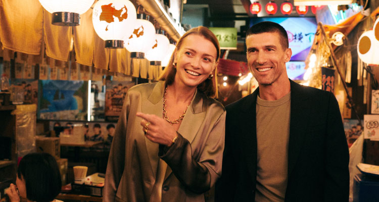 Two people standing in a bustling  market in Japan, surrounded by hanging lanterns.
