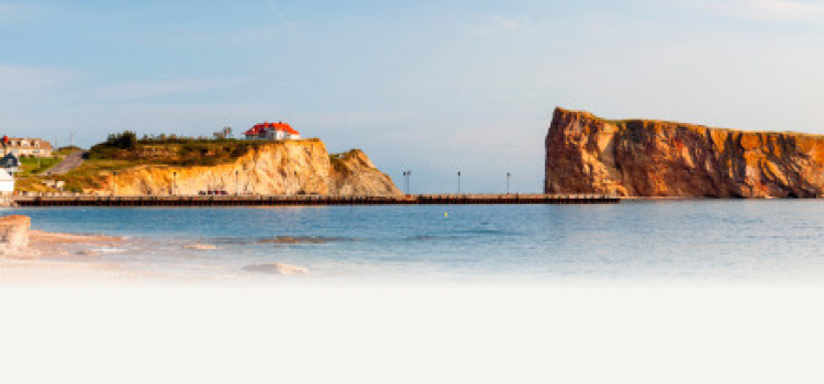A coastal landscape with a house on a cliff and a prominent rock formation in the water.