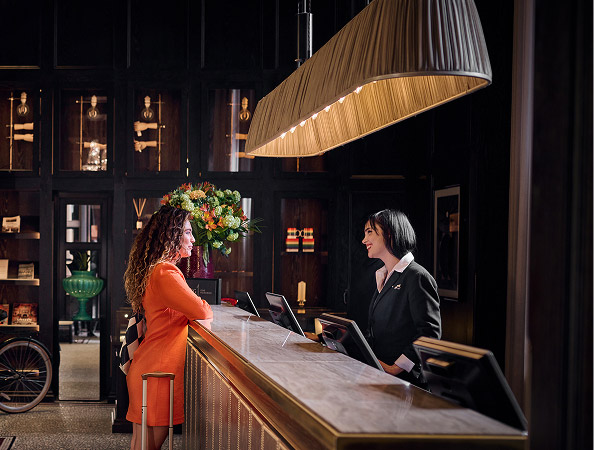 Guest at hotel front desk speaking with staff at check-in counter.