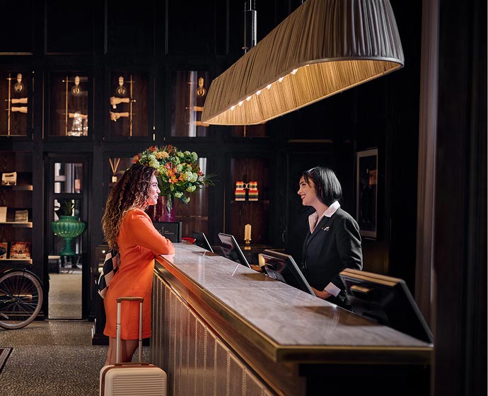 Guest at hotel front desk speaking with staff at check-in counter.