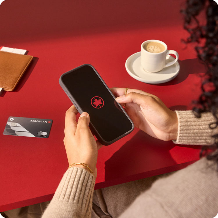Hands holding a smartphone with Air Canada's Maple leaf rondelle on a red table