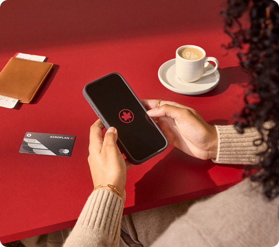 Hands holding a smartphone with Air Canada's Maple leaf rondelle on a red table