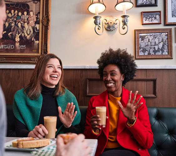 Two women laughing while drinking coffee in a cafe
