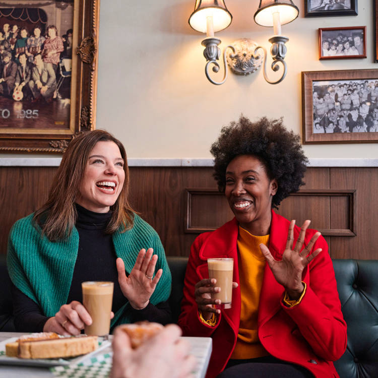Two women laughing while drinking coffee in a cafe